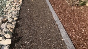 A pathway with a mix of gravel and mulch, bordered by rocks and plants, leading to a building with a beige exterior. - A Little Luxury near the AFA and Ford Amphitheater (Colorado Springs)