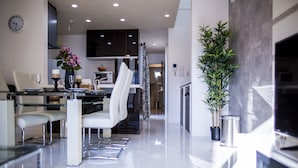 A modern kitchen with a dining area, featuring a glass table, white chairs, and a potted plant.