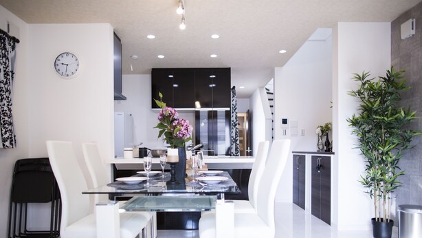 A modern kitchen with dark cabinets, a central island, and a dining area with white chairs and a glass table.