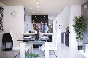 A modern kitchen with dark cabinets, a central island, and a dining area with white chairs and a glass table.