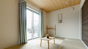 A minimalist room with tatami flooring, a sliding glass door, a small table with a vase, and a framed picture on the wall.