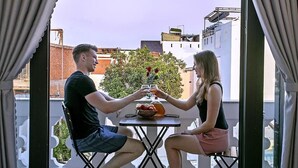 A couple seated at a table on a balcony with a city view, a fruit bowl, and a glass of drink. - Focus Homestay (Da Nang)