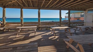 Een houten terras met picknicktafels, met uitzicht op een strand.