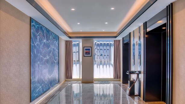 Un vestíbulo de hotel moderno con suelo de mármol, una gran obra de arte a la izquierda y un mostrador de recepción a la derecha.
