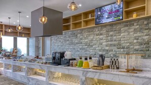 Una barra de desayuno moderna con encimera de mármol, máquinas de café y una pantalla de televisión mostrando un programa.