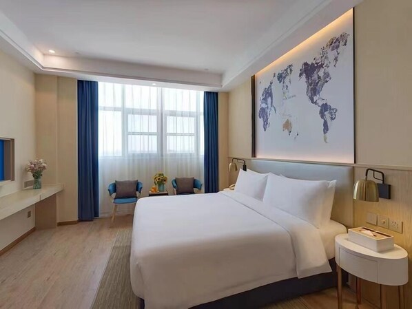 A hotel room with a large bed, a desk with a chair, a world map on the wall, and a window with curtains.