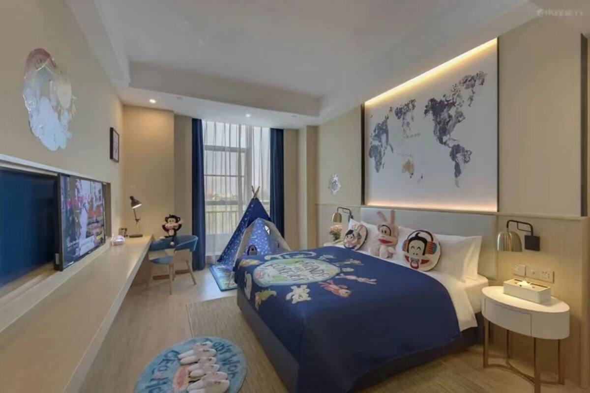 A hotel room with a large bed, a desk, a chair, a world map on the wall, and a small play tent.