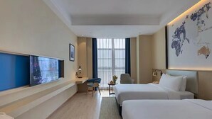 Habitación de hotel con dos camas, un escritorio, una silla, un televisor y un mapa mundial en la pared.