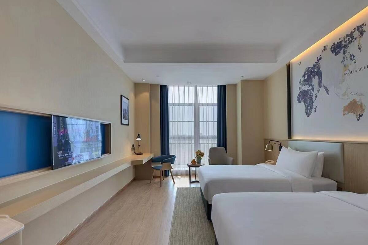 A hotel room with two beds, a desk, a chair, a TV, and a world map on the wall.