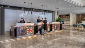 Un moderno mostrador de recepción con un diseño único, que incluye un mapa del mundo y maletas. Tres recepcionistas atienden a los huéspedes.