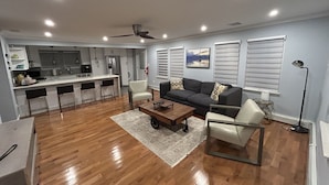 A modern living room with a wooden floor, a sofa, a coffee table, and a dining area with bar stools.