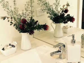 A bathroom with two white vases of flowers, a white sink, a mirror, and a soap dispenser. - Great Ocean Walk Retreat (Glenaire)