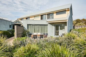 A modern two-story house with a large garage, a covered patio, and a well-maintained garden with various plants.