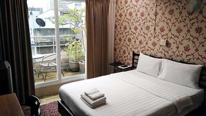 A hotel room with a bed, a chair, a small table, and a view of the outside. - 14 Plus 1 Hotel (Bangkok)