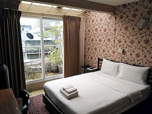 A hotel room with a bed, a chair, a small table, and a view of the outside. - 14 Plus 1 Hotel (Bangkok)