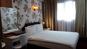 A hotel room with a bed, a desk with a chair, a nightstand, and a wall-mounted lamp. - 14 Plus 1 Hotel (Bangkok)