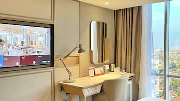 A hotel room with a bed, desk, chair, TV, and a large window with a city view.