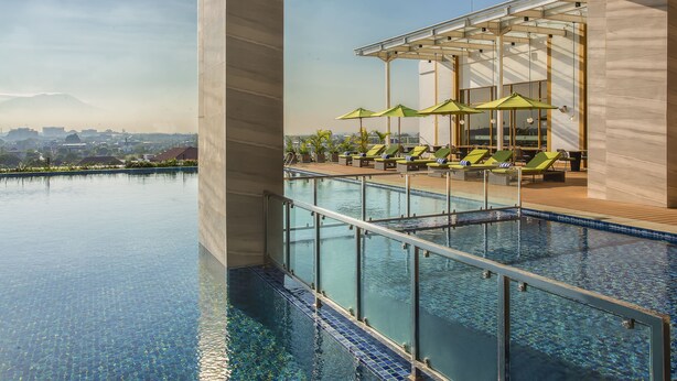 A rooftop infinity pool with a clear view of the cityscape, surrounded by lounge chairs and umbrellas. - Swiss-Belhotel Solo (Surakarta)