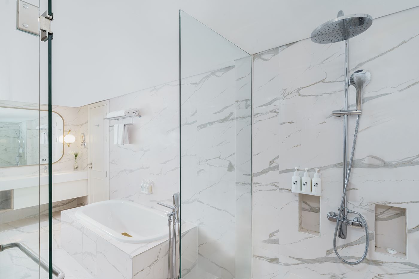 A modern bathroom with a glass-enclosed shower, a standalone bathtub, and a marble-tiled wall.