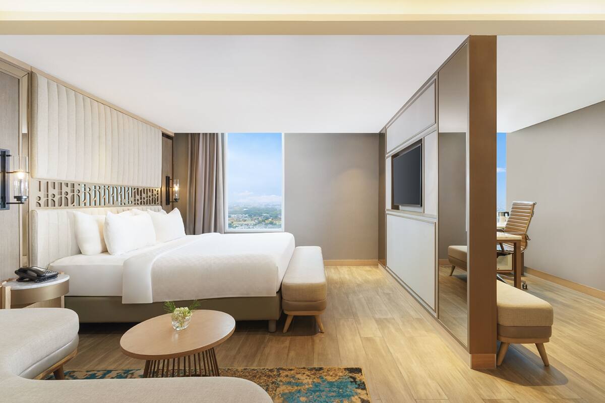 A modern hotel room with a large bed, a sitting area with a coffee table, a TV, and a view of the city.