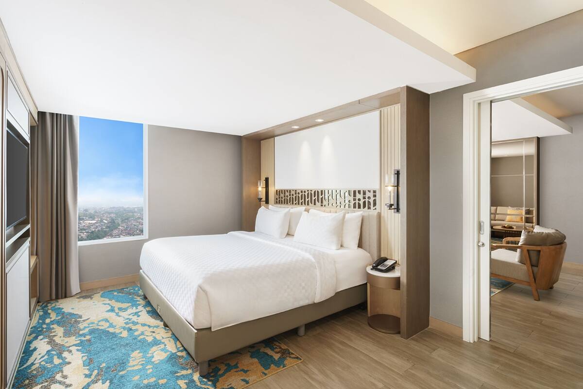 A modern hotel room with a large bed, a bedside table, a nightstand, and a view of the city.