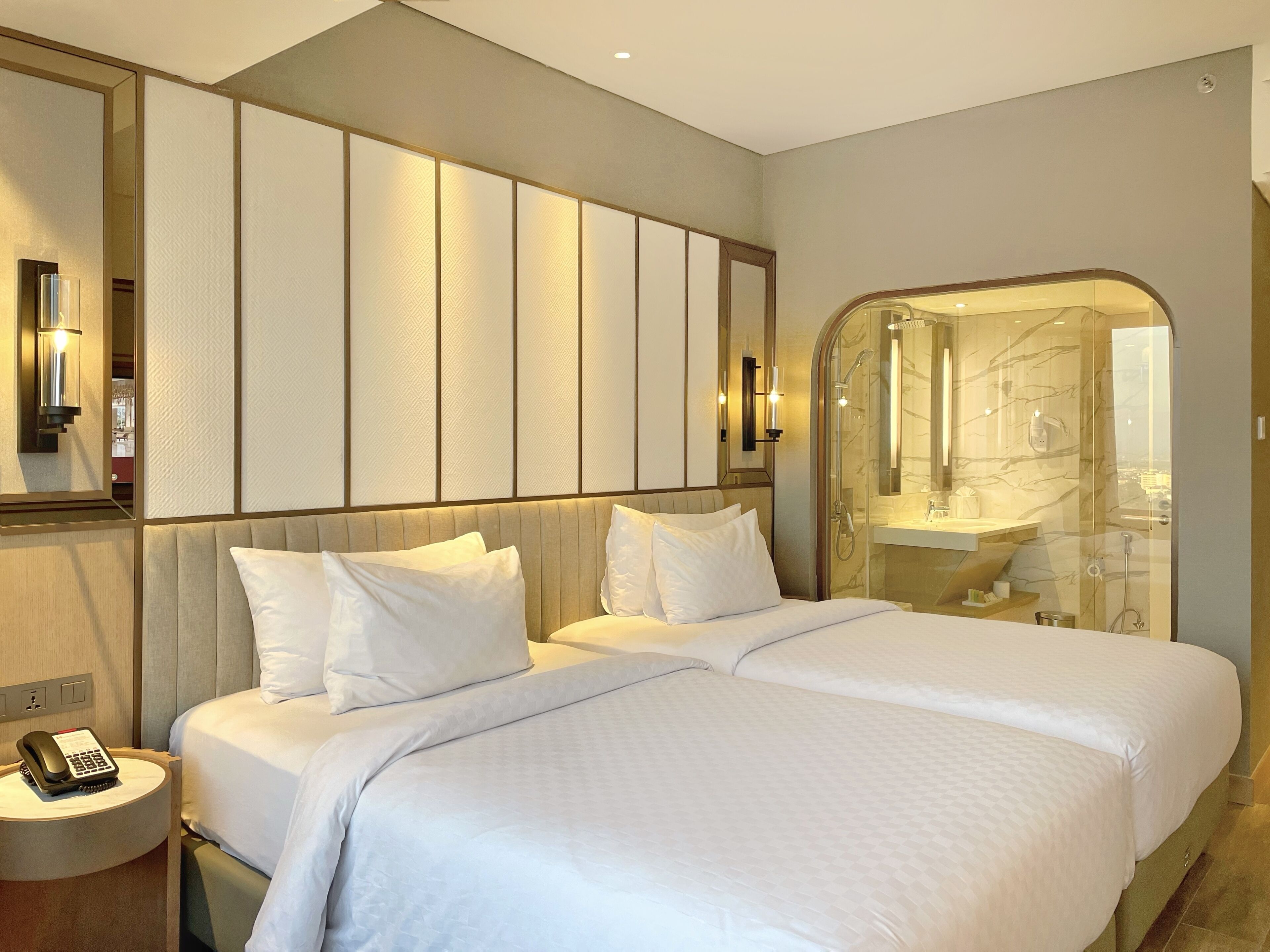 A hotel room with a large bed, a bedside phone, a mirror, and a bathroom with a glass shower enclosure.