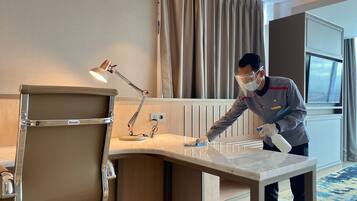 Habitación de hotel con un escritorio, una lámpara y una persona limpiándolo.