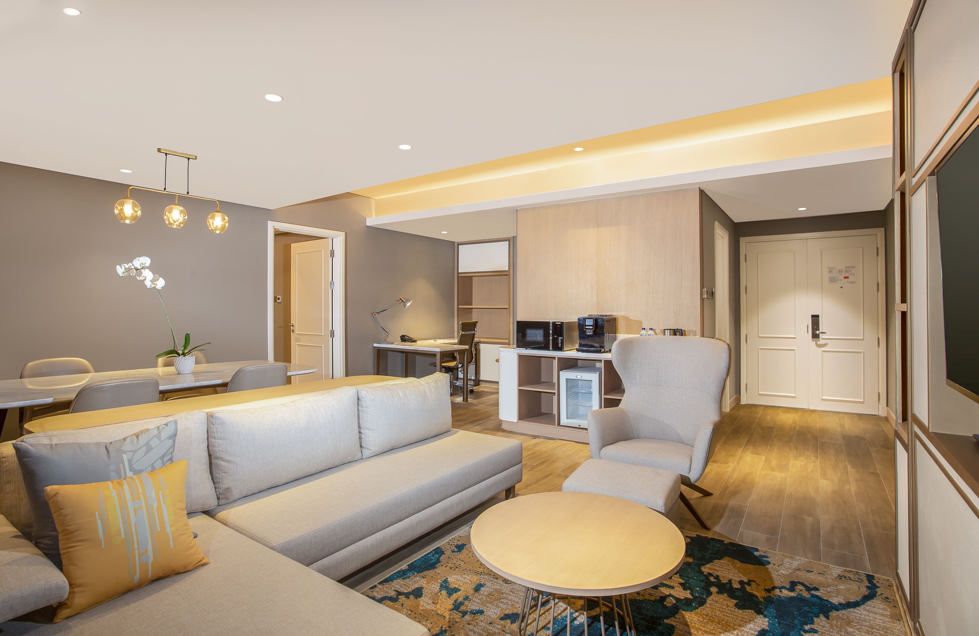 Una sala moderna con un sofá, sillones, una mesa de centro y un comedor con sillas y una mesa. Hay una zona de cocina con electrodomésticos y un refrigerador.