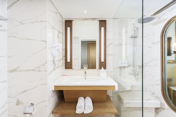 A modern bathroom with a marble wall, a wooden vanity, a glass shower enclosure, and a mirror with vertical light fixtures.