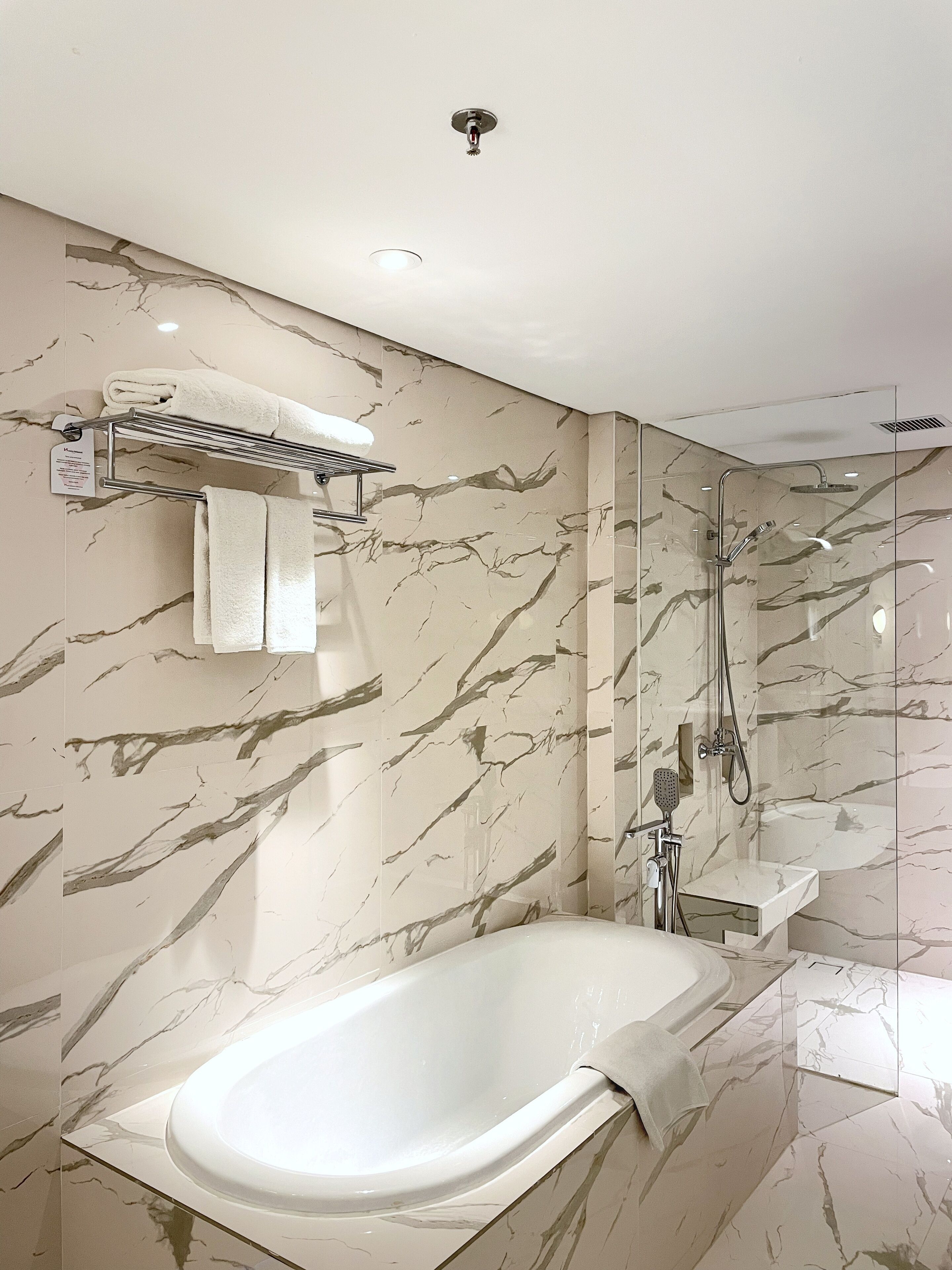 A modern bathroom with a freestanding bathtub, a glass-enclosed shower, and marble-patterned walls.
