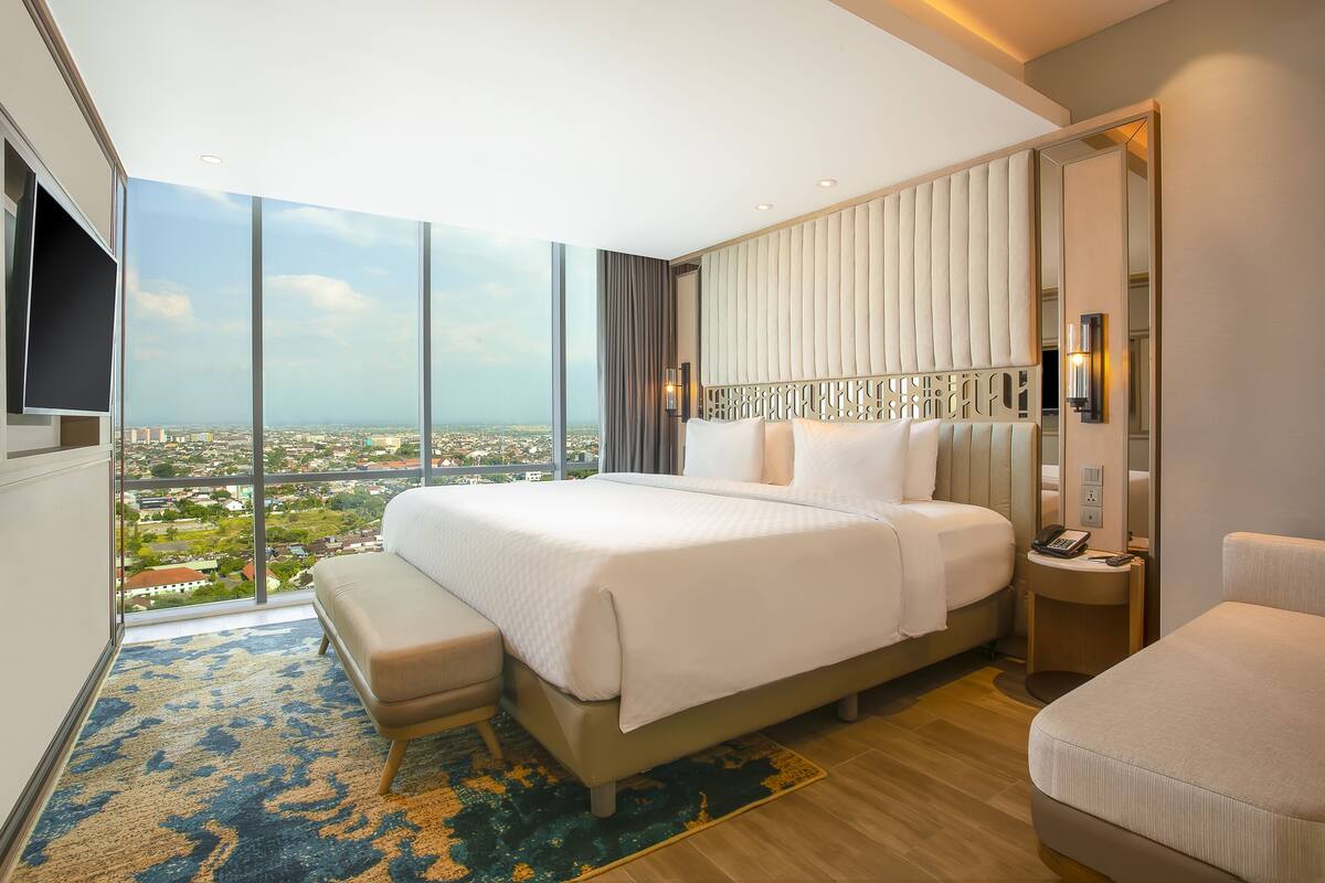 A modern hotel room with a large bed, a seating area, and a city view.