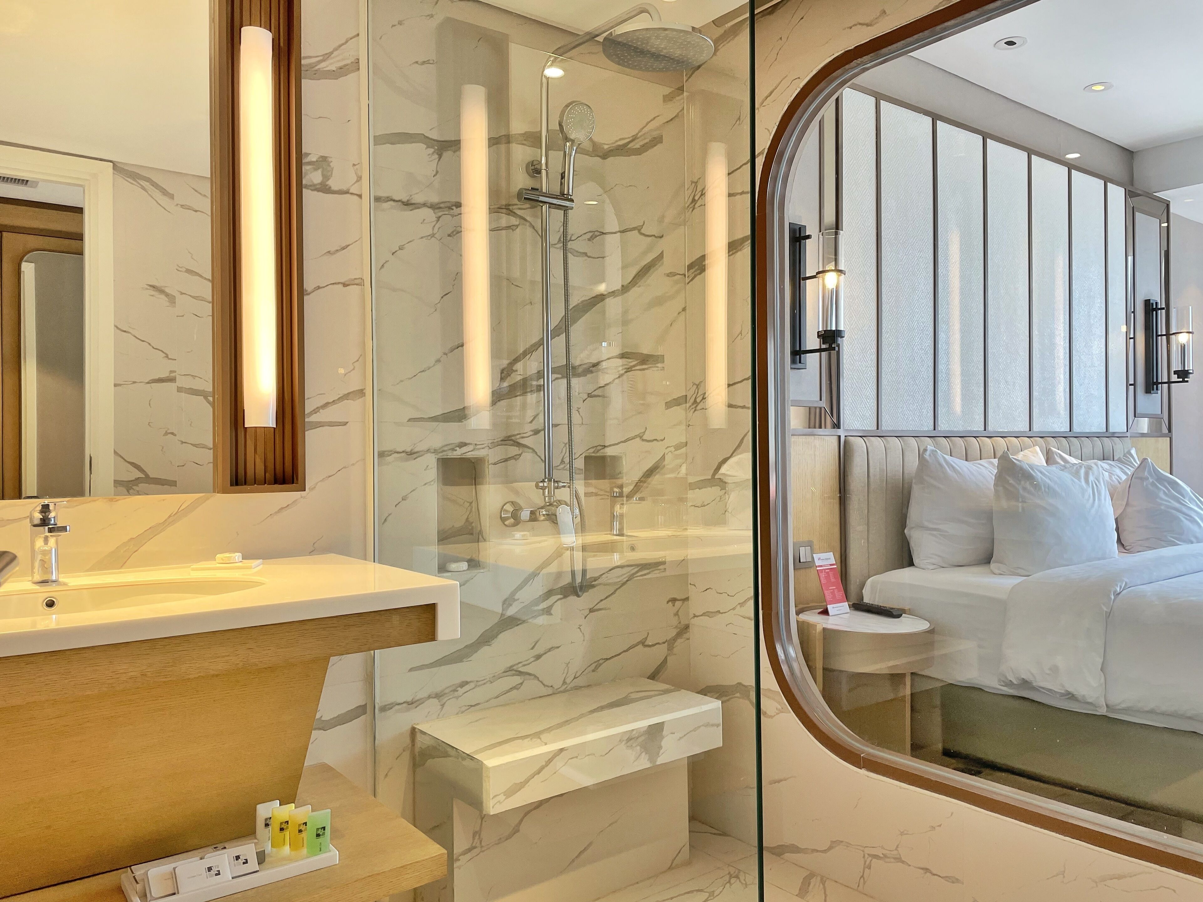 Un baño moderno con ducha envuelta en vidrio, paredes de mármol y un tocador con lavamanos y espejo.