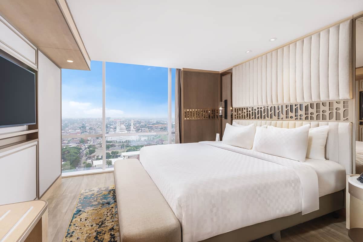 A modern hotel room with a large bed, a TV, and a city view.