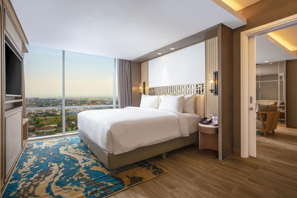 A modern hotel room with a large bed, a nightstand, and a view of the city.