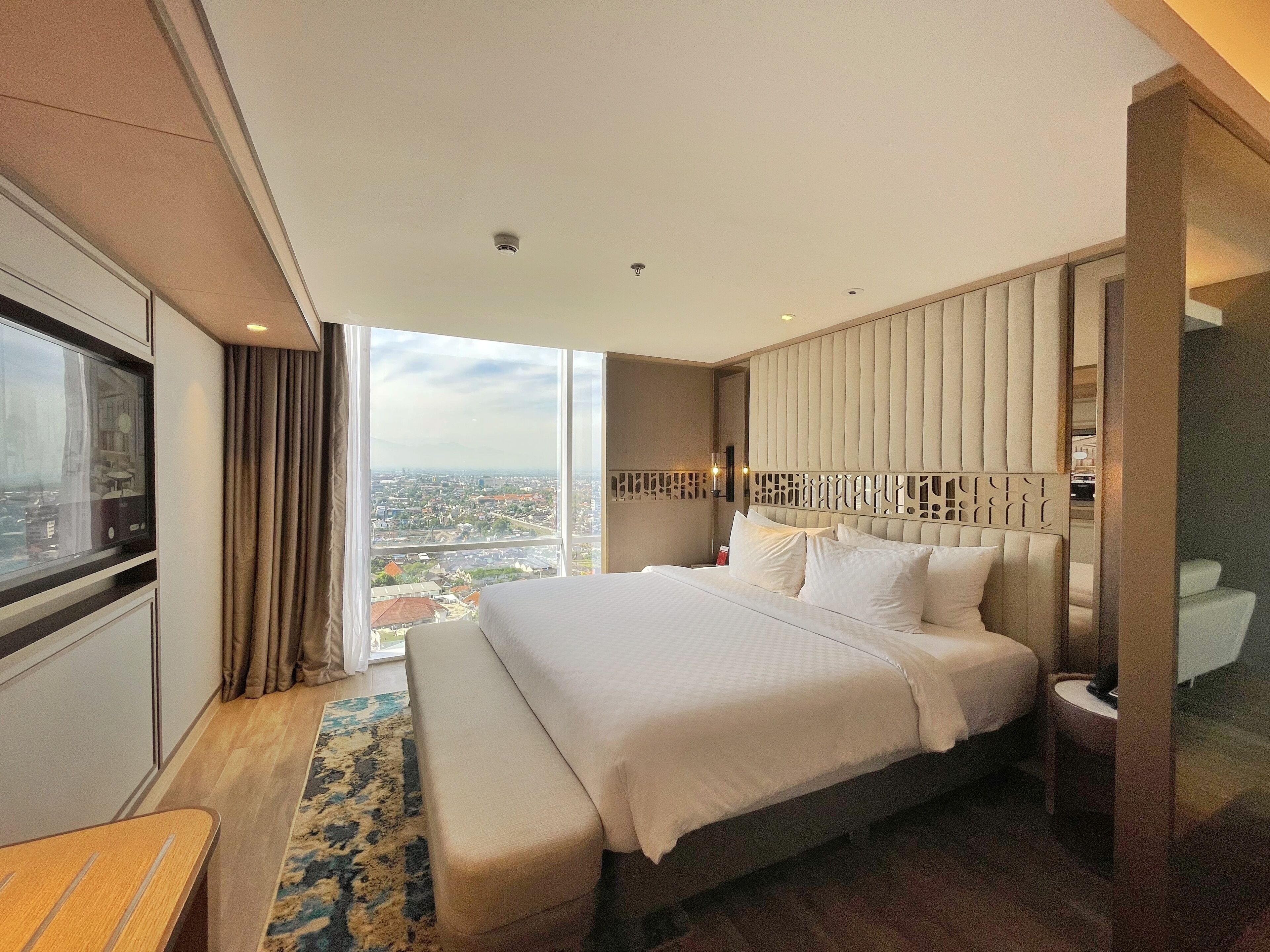 A modern hotel room with a large bed, a view of the city, and a small table.
