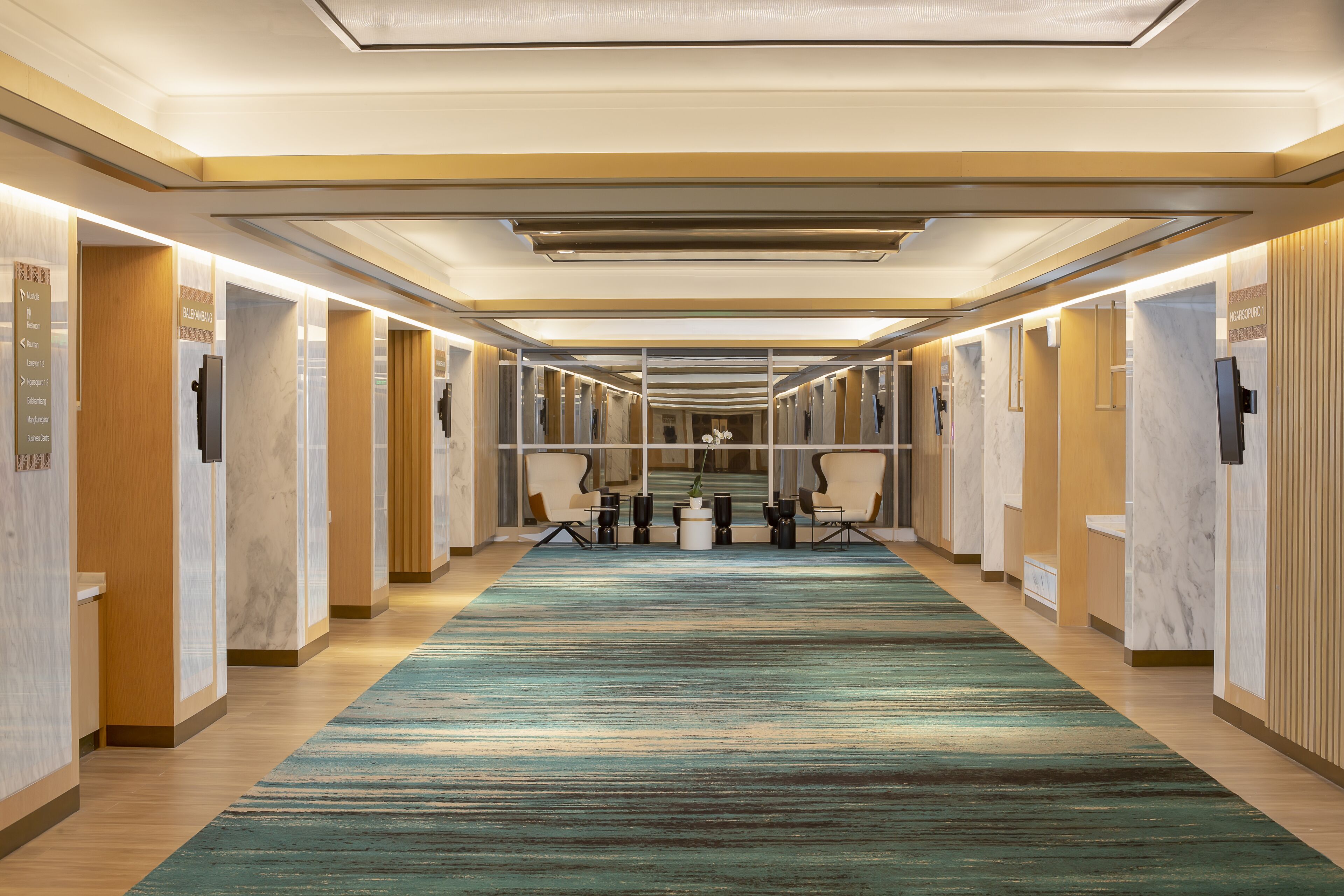 A hotel corridor with a carpeted floor, wooden paneling, and a series of doors leading to rooms.