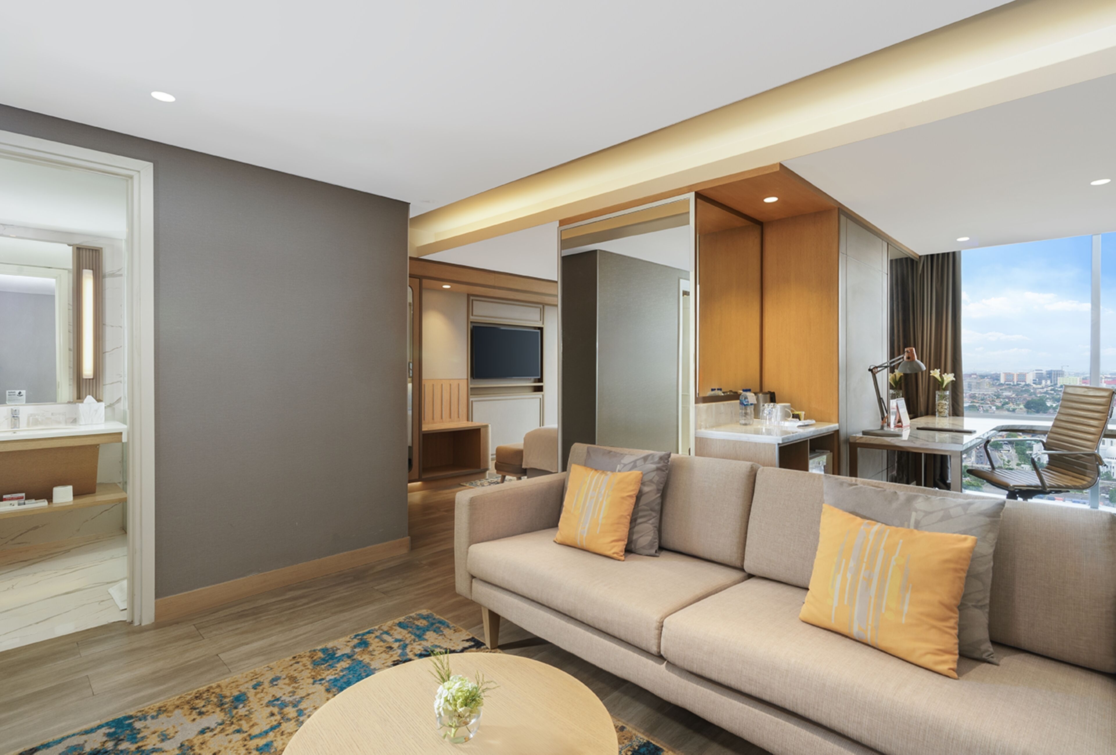A modern hotel room with a sofa, a coffee table, and a view of the city.