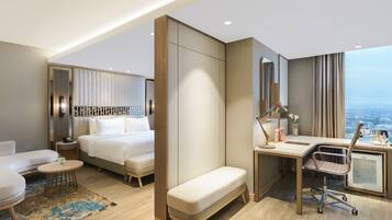 A modern hotel room with a bed, a desk, a chair, a bench, and a view of the city.