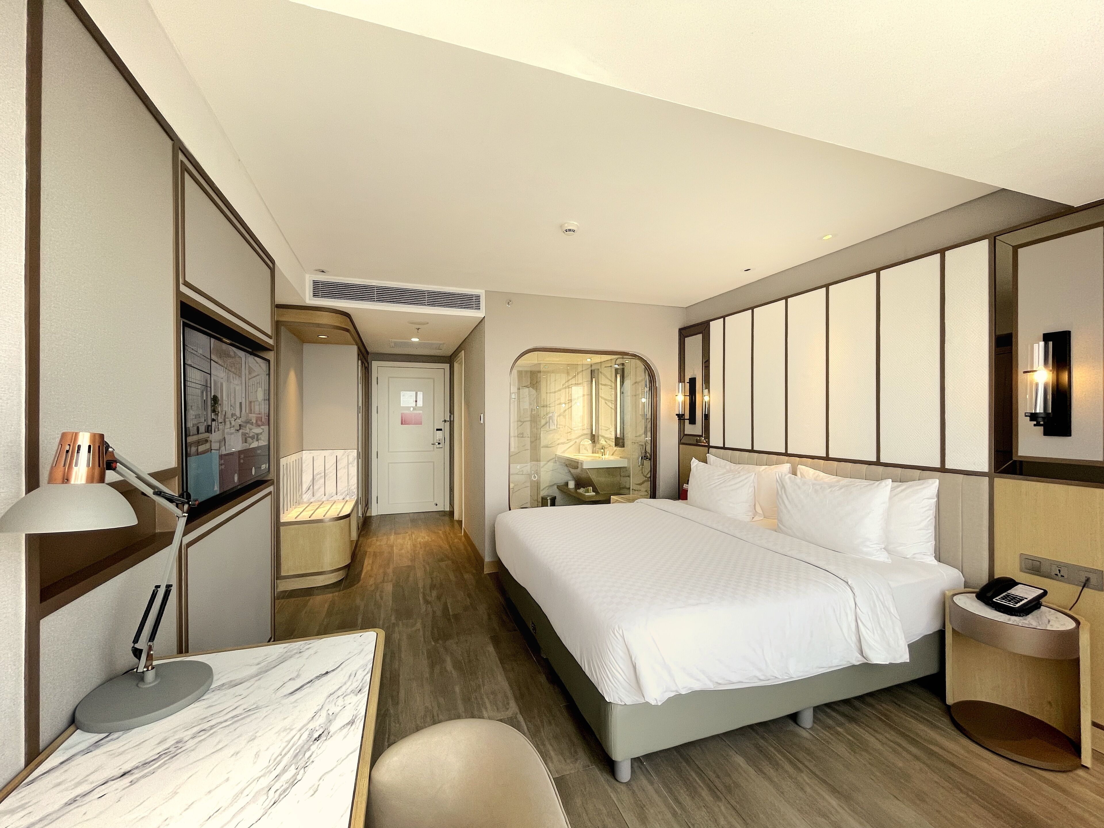 A hotel room with a bed, bedside table, lamp, and a view of the bathroom.