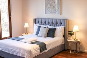 A neatly made bed with a grey upholstered headboard, two bedside lamps, and a framed artwork above the bed.