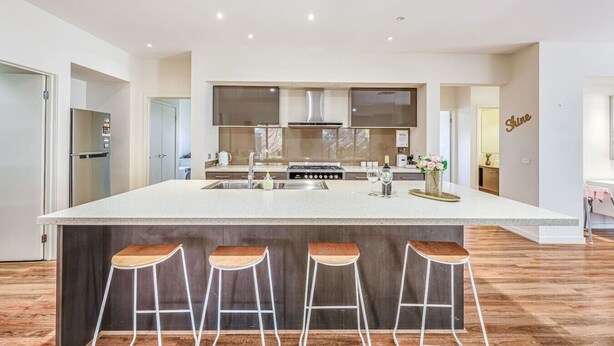 Una cocina moderna con una isla grande, taburetes de bar, electrodomésticos de acero inoxidable y un jarrón decorativo.