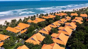 A resort with multiple buildings, each with a red-tiled roof, situated near a beach with palm trees and the ocean. - Luxury Villas - Villa Danang Beach (Da Nang)