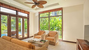 A spacious living area with wicker furniture, a ceiling fan, and large windows offering a view of greenery. - Luxury Villas - Villa Danang Beach (Da Nang)