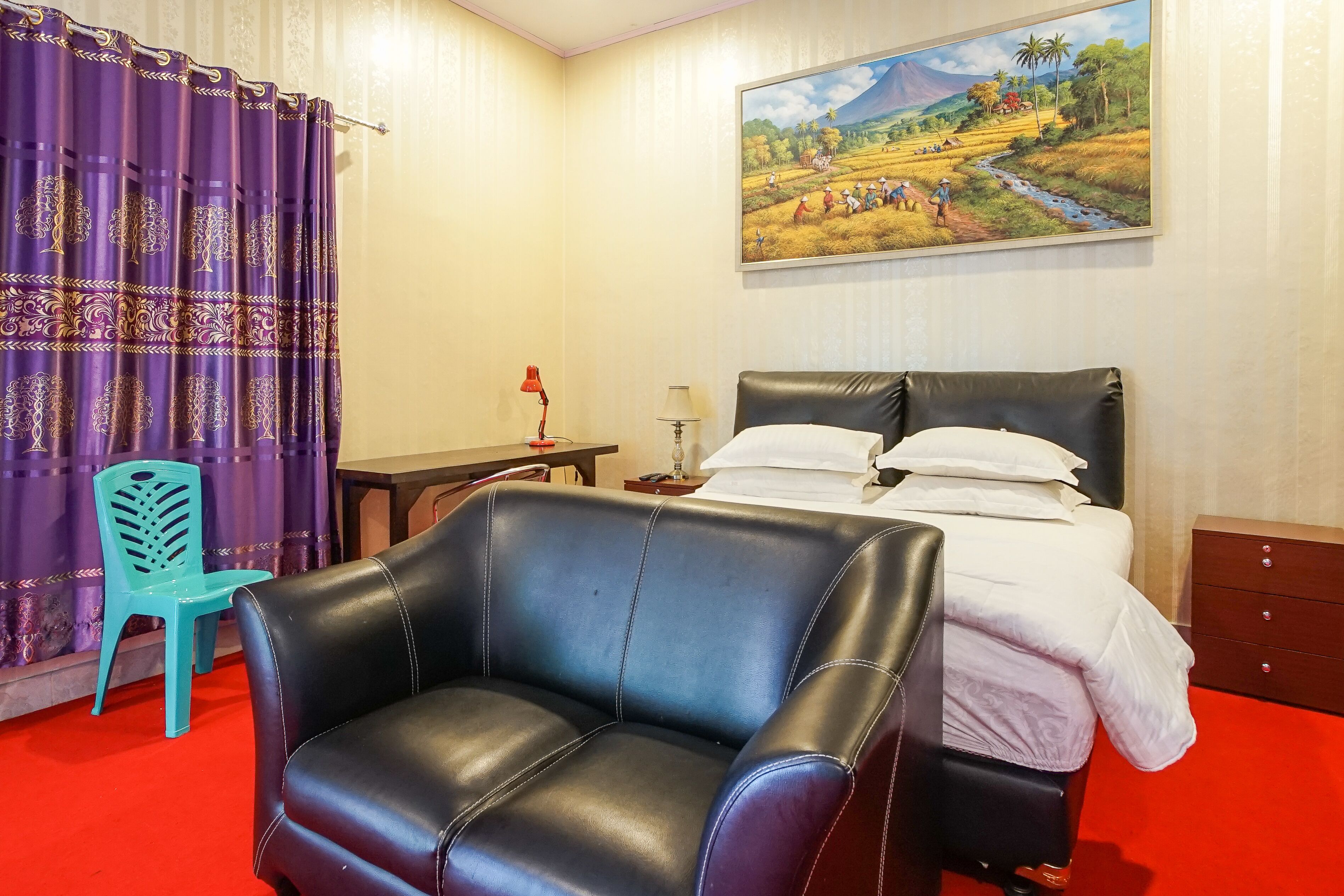 Quarto de hotel com uma cama, uma poltrona de couro preto, uma poltrona turquesa, um quadro na parede e um tapete vermelho.