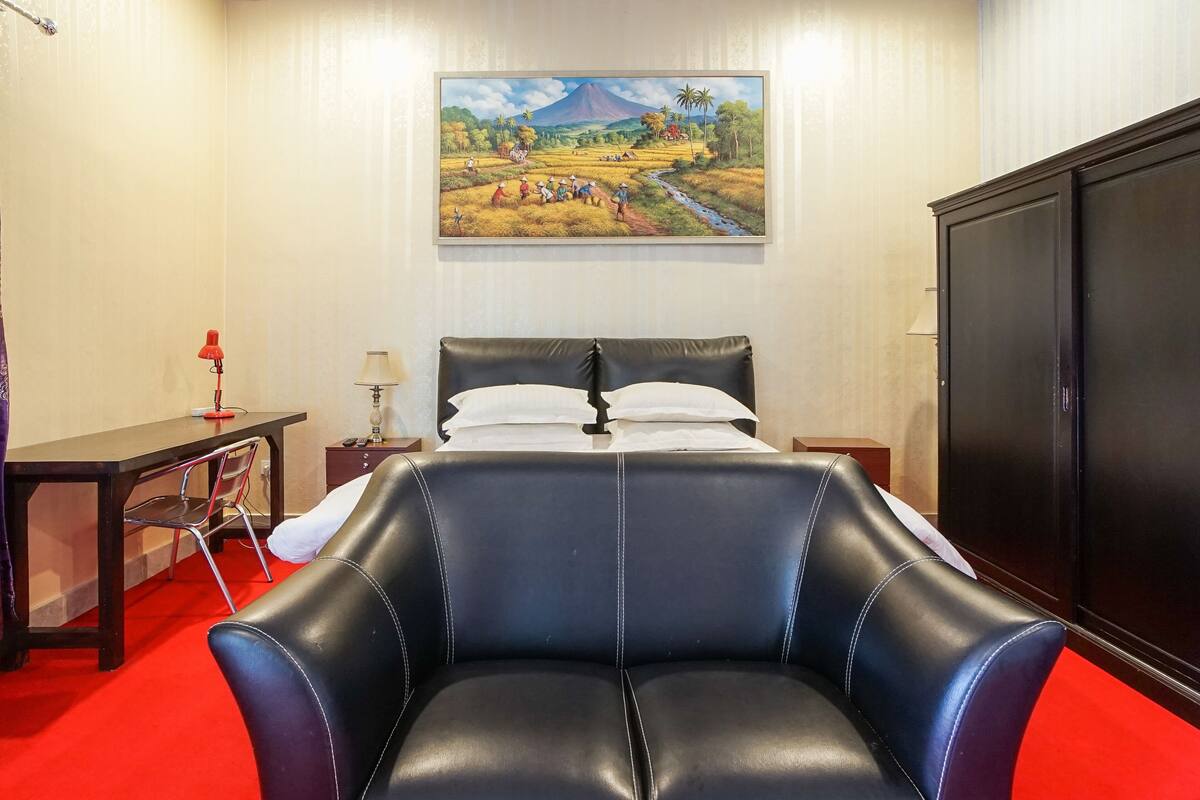 Una habitación con cama, escritorio, silla, lámpara y un cuadro en la pared.