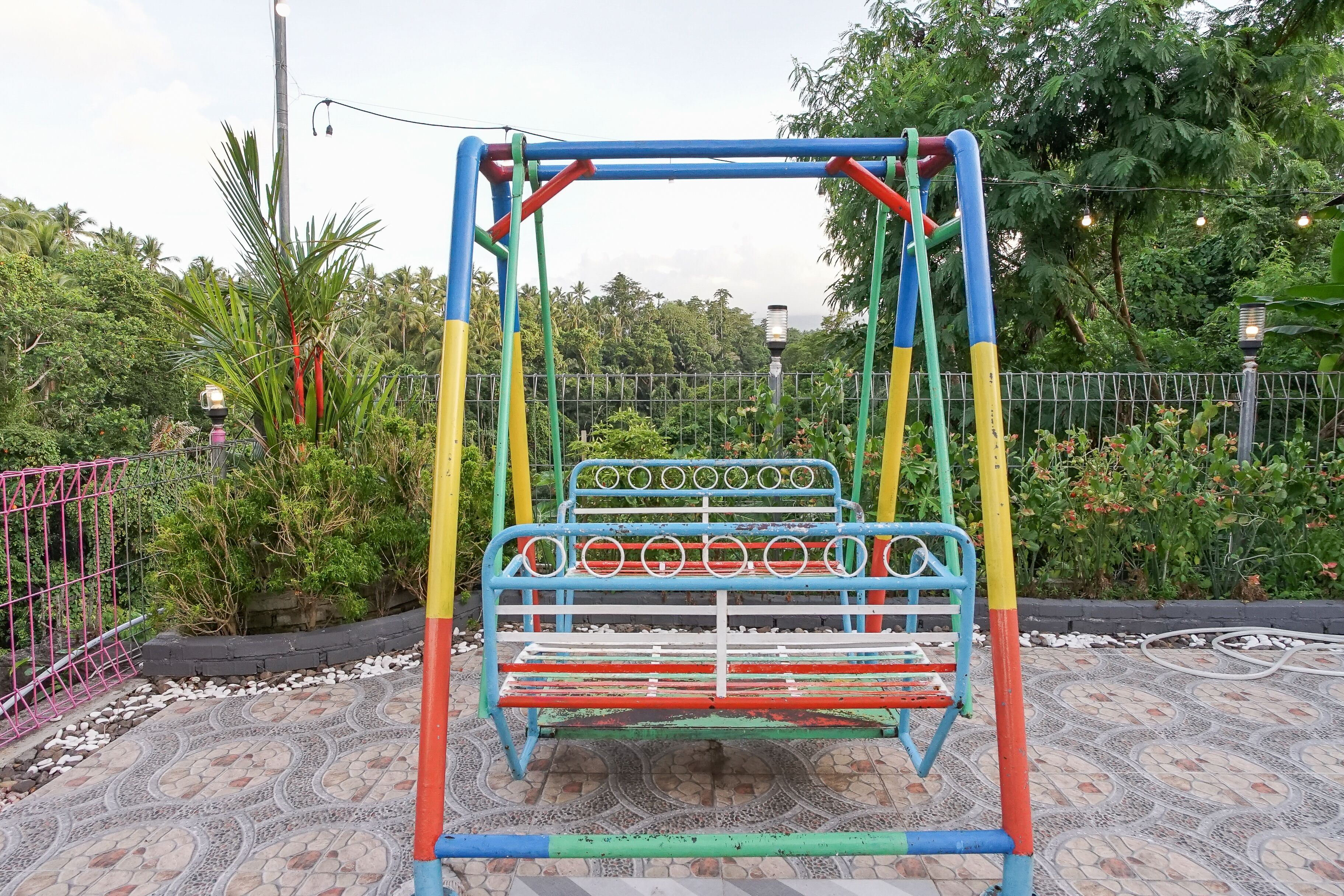 A playground with colorful equipment, surrounded by a fence and greenery.