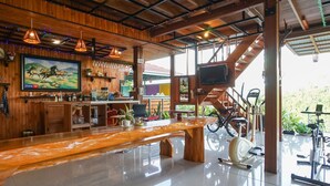 A spacious room with a wooden bar area, exercise equipment, and a television. - Villa Robert (Manado)