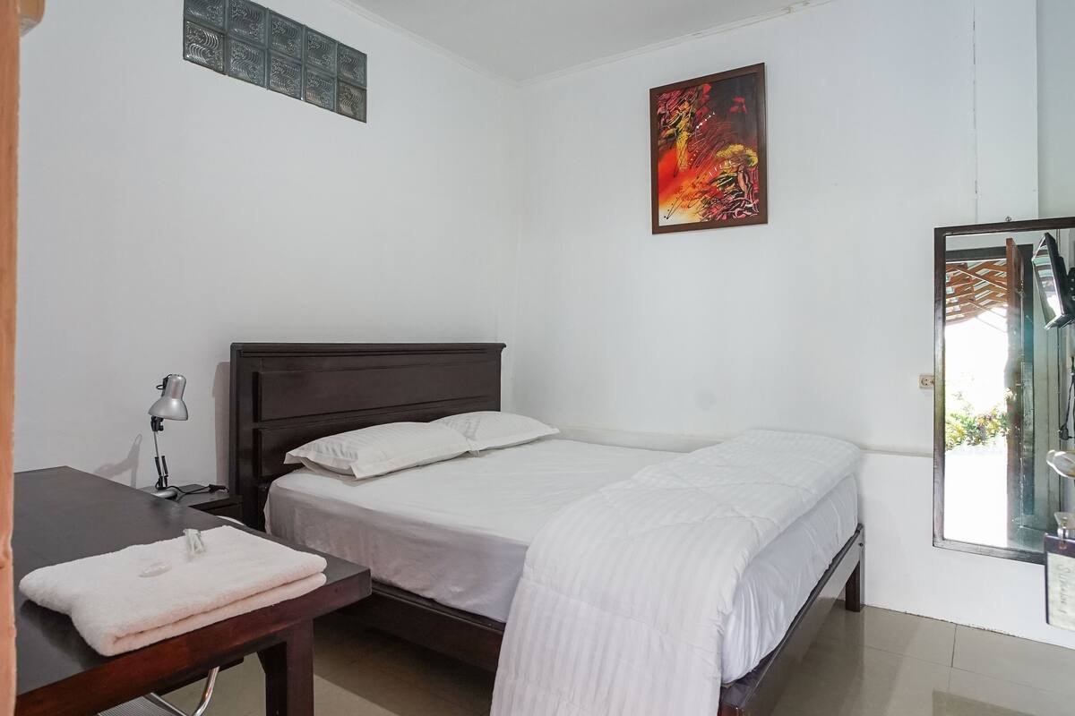 Un dormitorio con cama, escritorio, silla, lámpara y ventana.