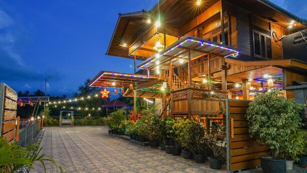 A wooden building with a covered outdoor area, potted plants, and string lights. - Villa Robert (Manado)