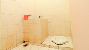 Une petite salle de bain carrelée, avec des toilettes à la turque, un seau rouge et un robinet fixé au mur.